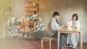 Pictured: Two women sit at a wooden table in a small one-room Japanese apartment, with plates and bowls in front of them. One women is in a sweater over a blue and white checked dress. The other woman wear loose-fitting grey sweats. Words on the image read 作りたい女と食べたい女 Tsukuritai Onna to Tabetai Onna. 