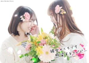 Title image for Yorita Miyuki's Kanojo no Kuchizuke Kansensuru Libido Short Movie (彼女のくちづけ感染するリビドー ショートムービー). Two young women with flowers in their hair hold a bouquet. The girls with long hair strokes the other girl's cheek as they smile gently.