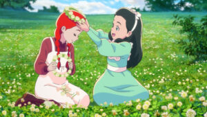 In a large field of flowers, two girls make flower crowns. A girl in a green dress and dark hair places a crown of flowers on the head of a red-haired girl in a white jumper dress over a dark read blouse who clutches a flower crown in here hands.