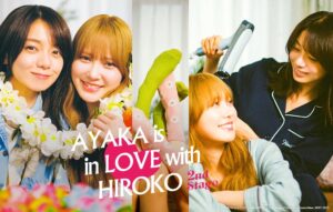 The promotional poster for season 2 of Ayaka Is in Love with Hiroko. On the left the actresses embrace, wearing Hawaiian patterns and a lei on the right Hiroko holds a blowdryer over Ayaka's hair. 