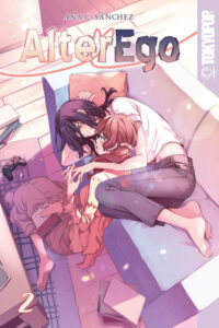 June, a woman with long black hair and wearing a t-shirt and jeans, is curled up sideways on a couch embracing Noel, who is sitting on the floor. They are looking at each other, smiling, and intertwining their fingers