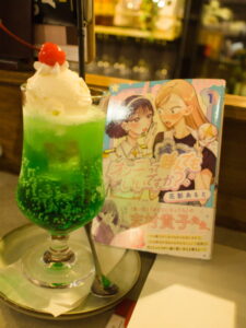 A green cream melon soda next to a copy of Unnie'tte Yondemo Ii Desuka? by Hanakage Alt at Anchor port rainbow Tokyo