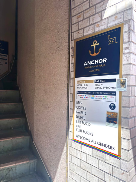 A photo of a staircase, with a placard on the wall for ANCOR rainbow port Tokyo, the Yuri cafe in Shinjuku Nichoume