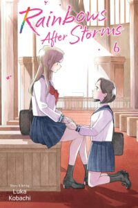Two girls in the same sailor-style school uniform of white blouse, dark blue skirt and red tie, in a church. One sits, as the other kneels in front of her, they hold hands looking deeply into one another's eyes.