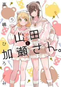 Two young woman stand before background of colorful cat face silhouettes, cups and toothbrushes. The taller, with dark brown hair wears a brown bear sweat jacket with ears on the hood. The short woman with collar-length blonde hair, wears pink and white stripes sweater and a white cat ear Alice band, as they hold toothbrushes and bathroom cups.