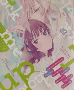 Among a forest of pastel colors and white and green words, a woman with pale pink hair embraces a woman with purple hair, who looks out at us.