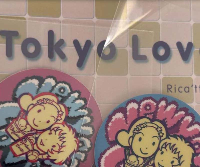 A close-up up Toyo Love - Rica 'tte Kanji!? cover and two Rica/x Miho pins.