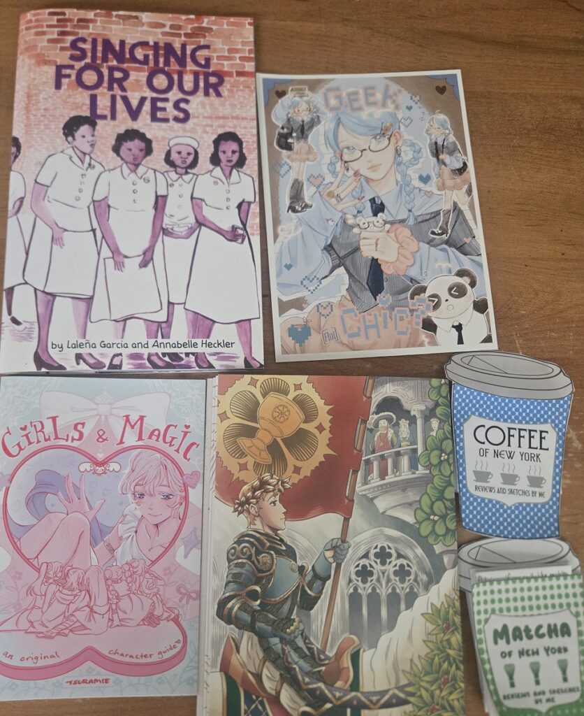 A photo of several small art comics, and illustrations from Flamecon