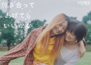 Saeko, a girl with long dyed light brown hair that has exposed black roots, holds her arm in a playfully familiar fashion around the shoulders Miwa, who is sporting a black bob. Both girls are smiling